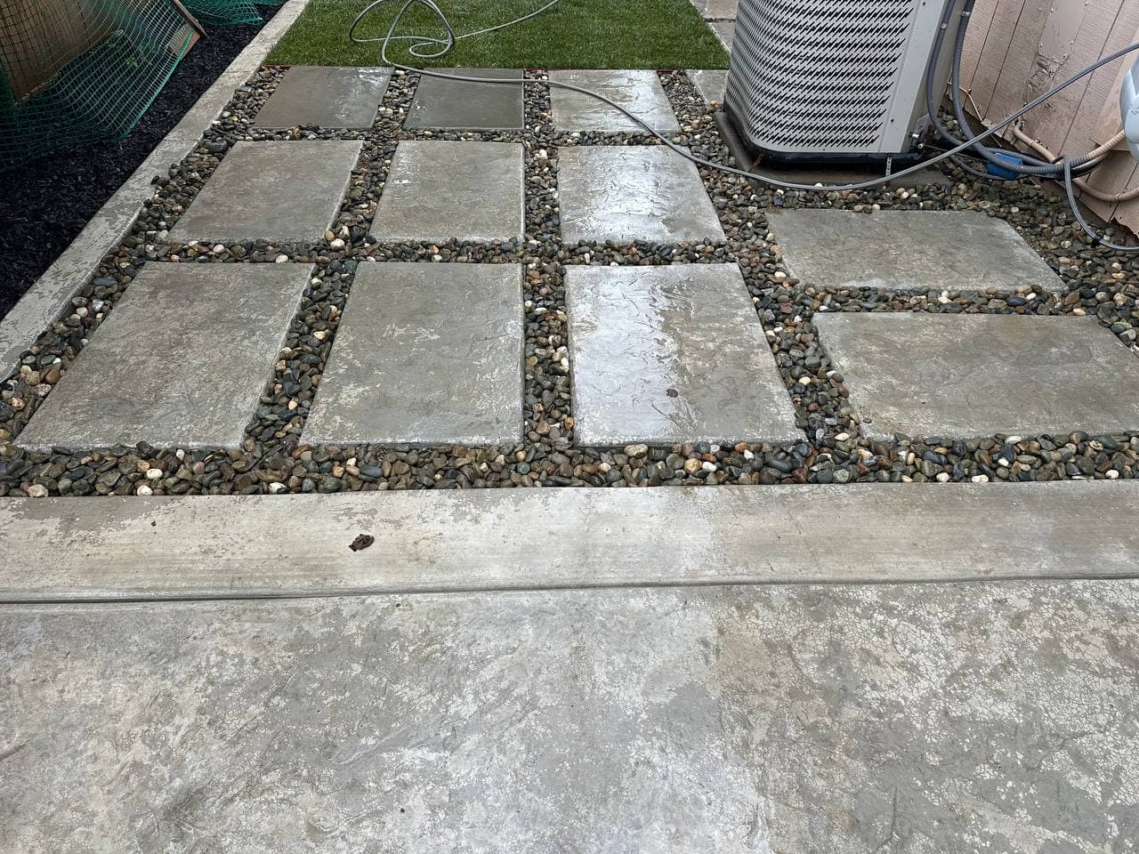 Concrete paver squares set into river rock landscaping