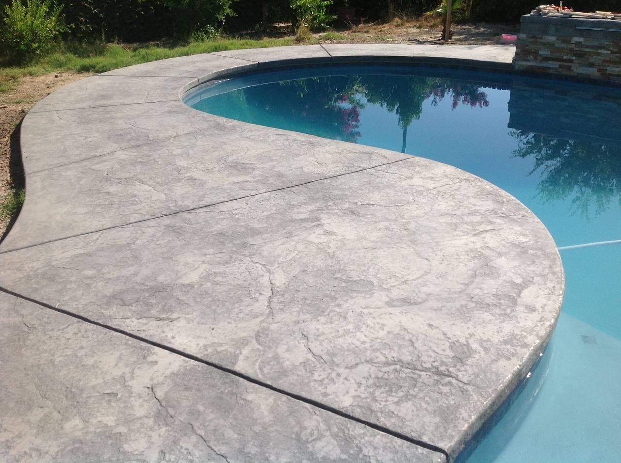 Curved gray stamped concrete pool deck beside a blue pool