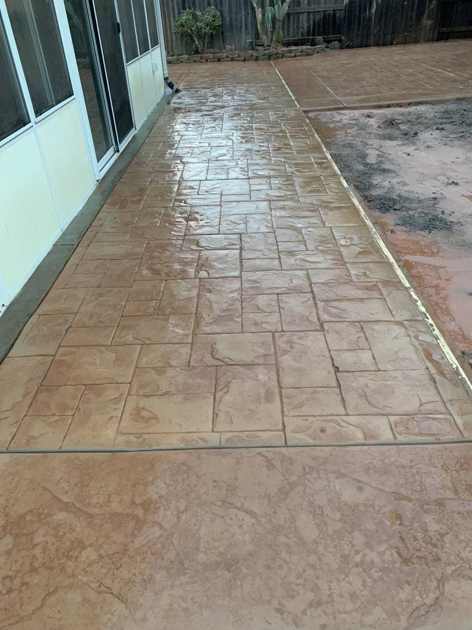 Tan ashlar stamped concrete patio along the back of a home